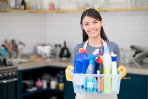Portrait of a housekeeper holding cleaning products while working at home and looking at the camera smiling
