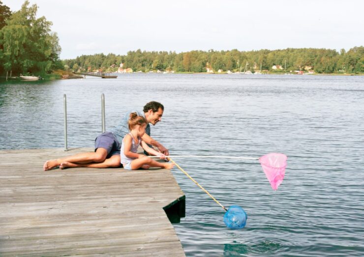 Isa ja tütar veekogu ääres suvel värviliste võrkudega kalu püüdmas.