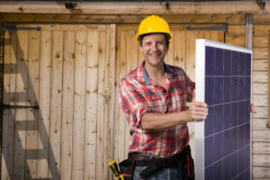 Portrait of smiling engineer holding solar panel in front of cabin