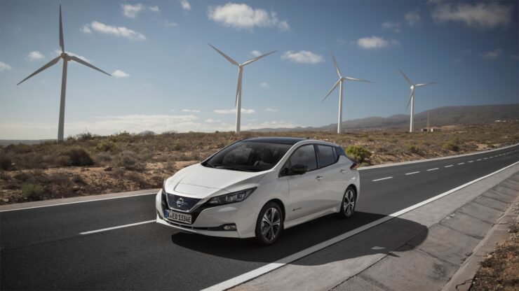 Fotol on nissan elektriline, mis sõidab teel. Taustal neli tuulikut.