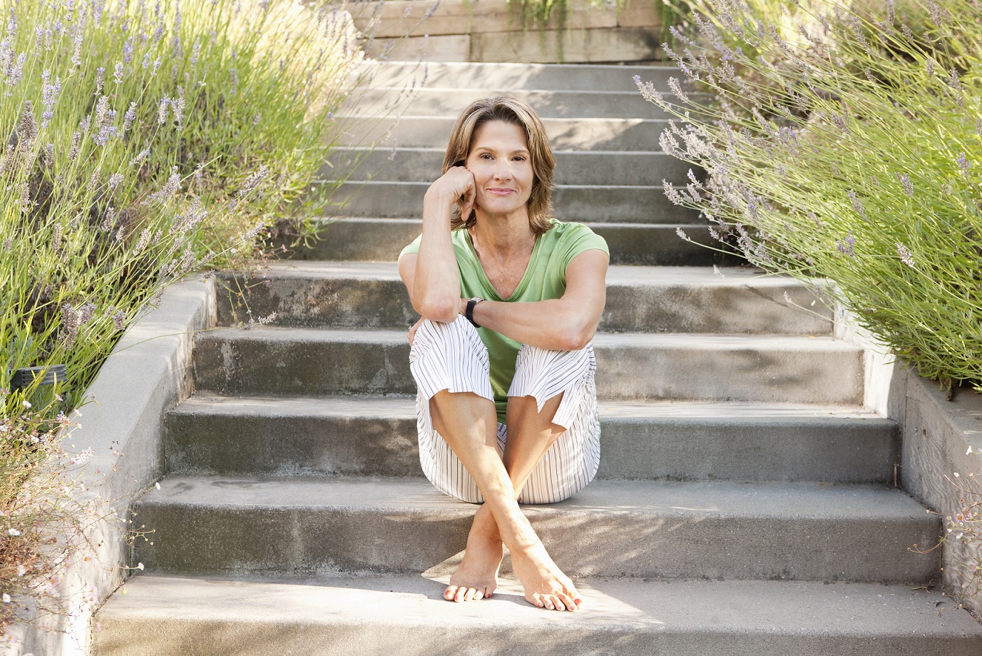 Smiling woman sitting barefoot on cement steps.