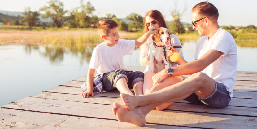 Kolmeliikmeline perekond: ema, isa ja poeg istuvad koos koeraga paadisillal ja mängivad. Suvine pilt