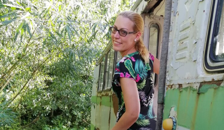 Naine kuskil looduses, seismas lagunenud bussi ukse peal ja naeratamas.