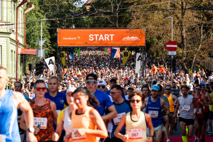 Pildil on sajad inimesed jooksmas Tallinna maratoni ning taga paistab suur Swedbanki bänner.