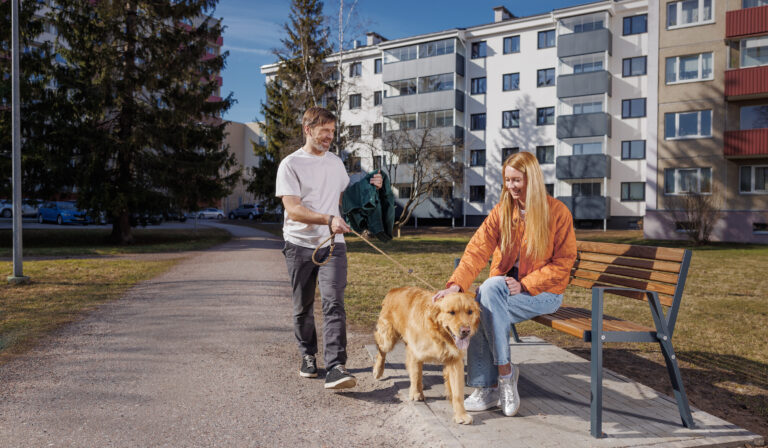 Mees ja naine jalutavad koos kortermajade ees koeraga