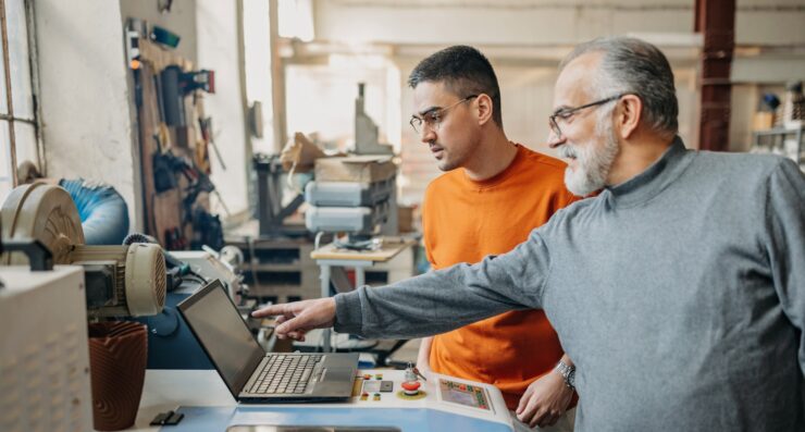 Kaks meest on kuskil töökojas, nende ees on arvuti ja vanem mees selgitab midagi sellelt arvutilt.