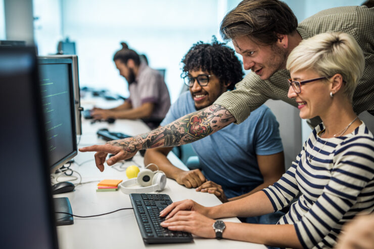 Kolm kolleegi istuvad ja vaatavad rõõmsate nägudega midagi lauaarvutist.
