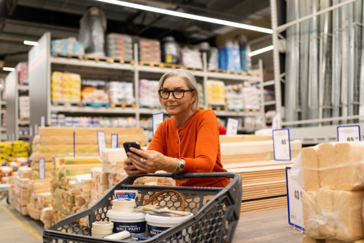Naine seisab ehituspoes. Käes telefon ja jalge ees ostukäru
