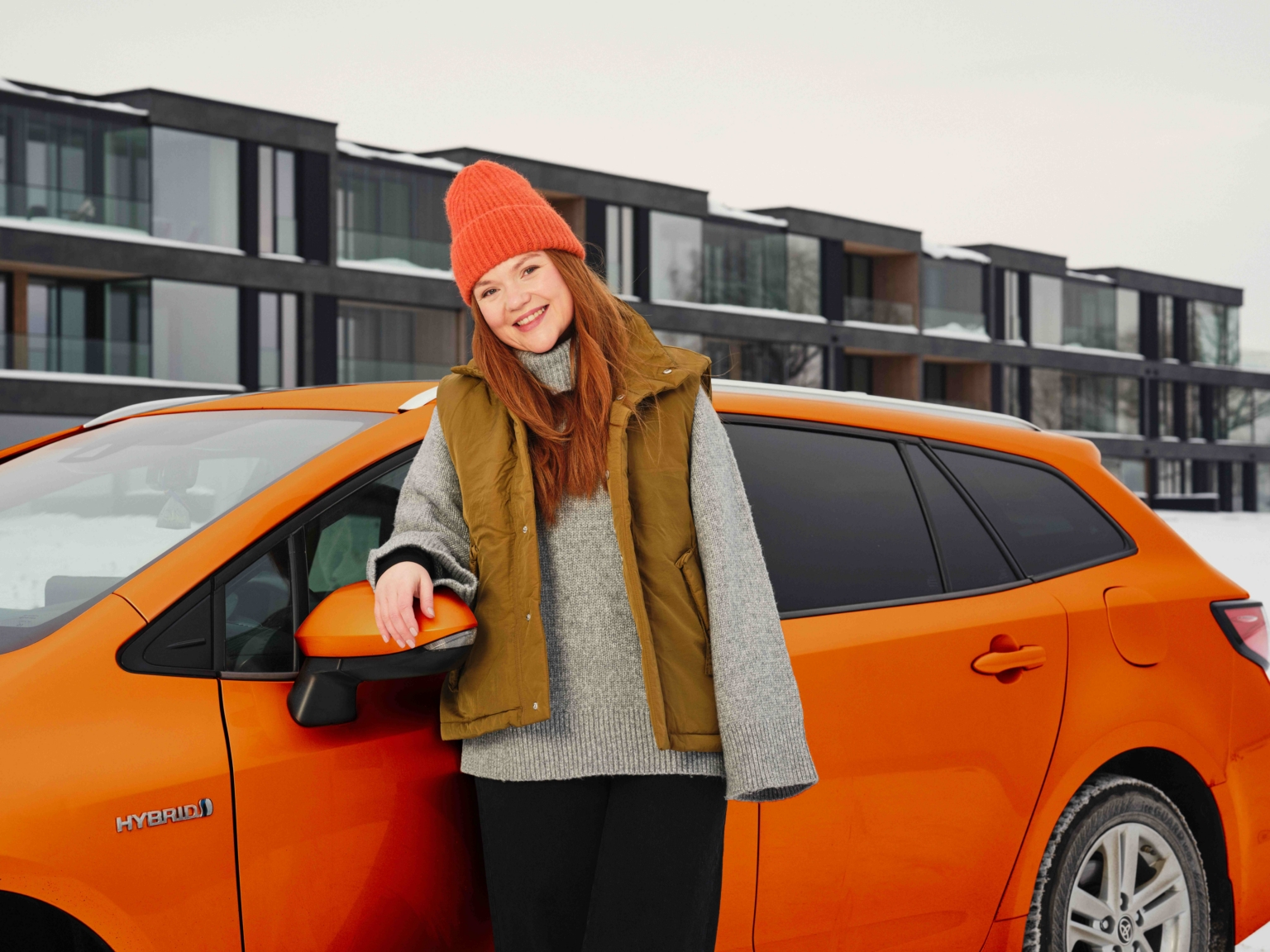 Noor naine seisab auto ees, taustal uusarendus