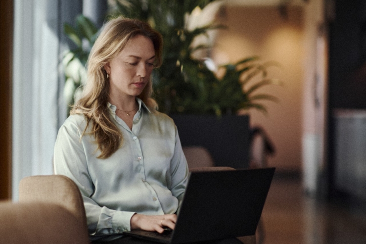 Naine istub kontoris tugitoolil. Tal on arvuti süles ning ta vaatab seda keskendunult.