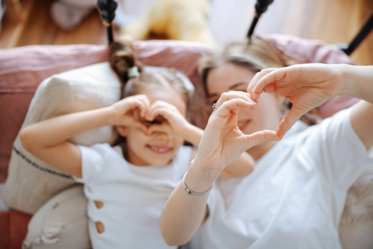 Pildil on ema oma tütrega diivanil kätega südant näitamas ja kaamerasse naeratamas