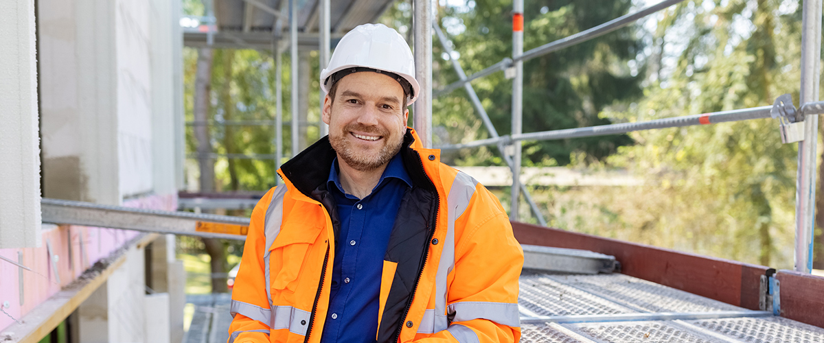 Tööriietes mees toetub tellingutele ja naeratab