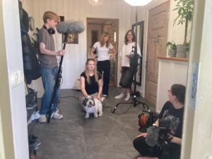 Filmivõtted. Näha on erinevaid noori, ühel käes suur mikrofon, teine hoolitseb valgustuse eest, kolmas tegeleb kaameraga ning kaks niisama jutustavad ja mängivad koeraga.