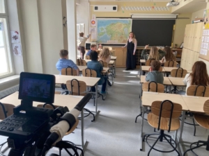 Pildil on filmivõtted Eesti koolis. Näha on lapsi koolipingis istumas ning õpetajat klassiruumi ees.