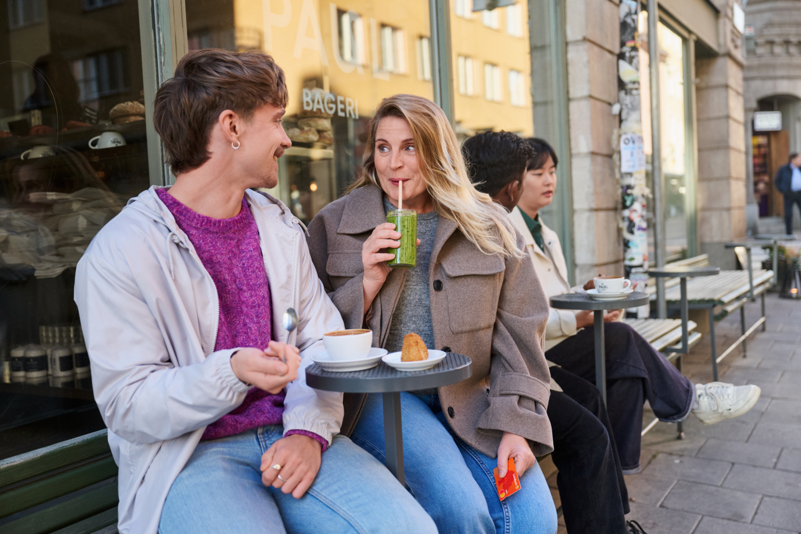 Naine ja noor mees istumas kohvikus. Naisel käes Swedbanki kaart ja smuuti
